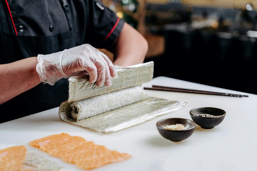 Chef's hands rolling maki sushi on a bamboo mat with salmon, cucumber and rice