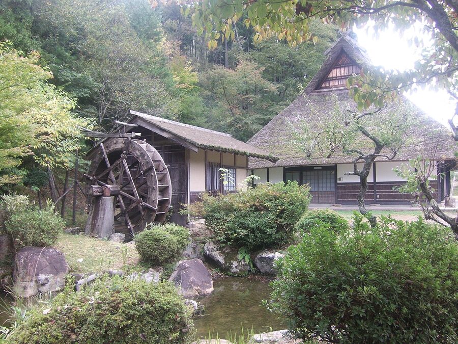 Close-up of a traditional Japanese thatched-roof farmhouse in Miyama with stone wall and wooden verandah