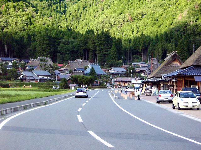 Thatched-roof houses spread across a gentle hillside in Miyama with rice paddies and forested mountains behind